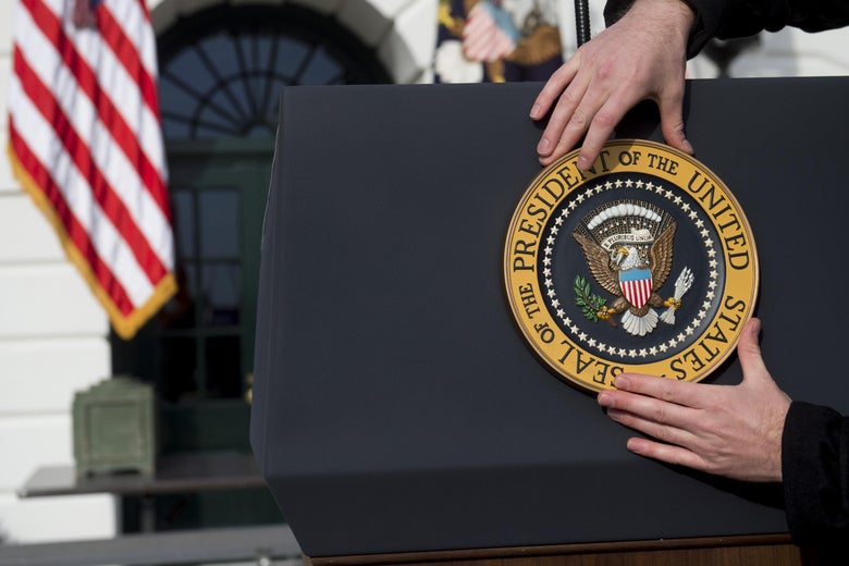 A staff member places the Presidential Seal on a podium on the South Lawn of the White House.